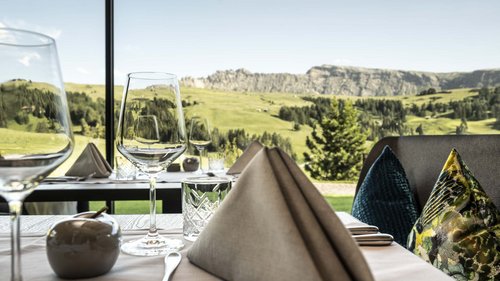 Hotel Schmung – Ihr Hotel auf der Seiser Alm Gedeckter Tisch mit Blick auf grüne Berge durch Fenster in Restaurant