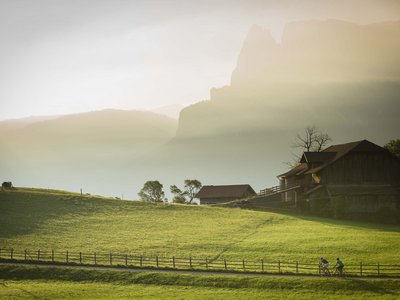 Hotel Schmung – Ihr Hotel auf der Seiser Alm Radfahrer fahren auf einem Weg neben Bauernhof in sonnenbeschienener Berglandschaft