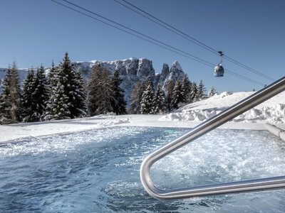 Hotel Schmung – Ihr Hotel auf der Seiser Alm Whirlpool in verschneiter Berglandschaft mit Seilbahn und klar blauem Himmel