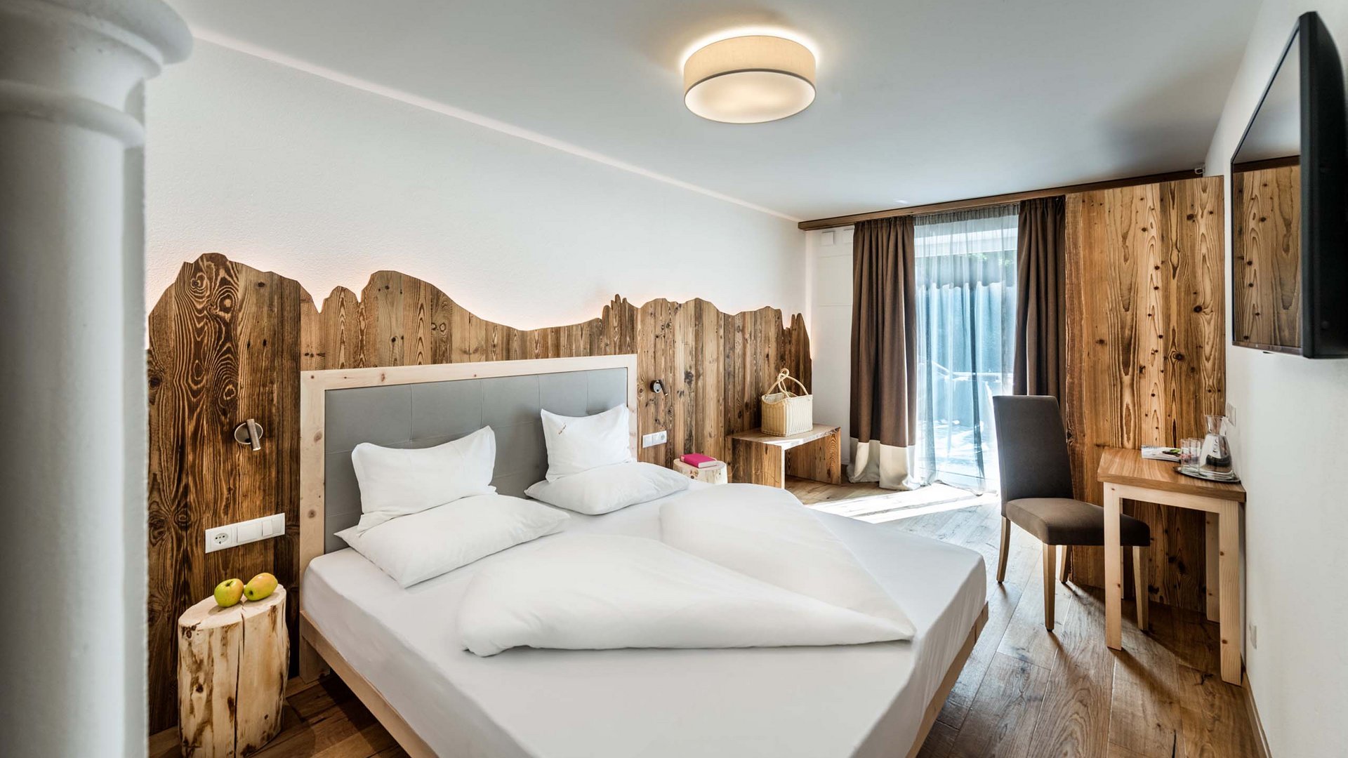 Hotel Schmung – Ihr Hotel auf der Seiser Alm Modernes Hotelzimmer mit Holzelementen und großem Bett
