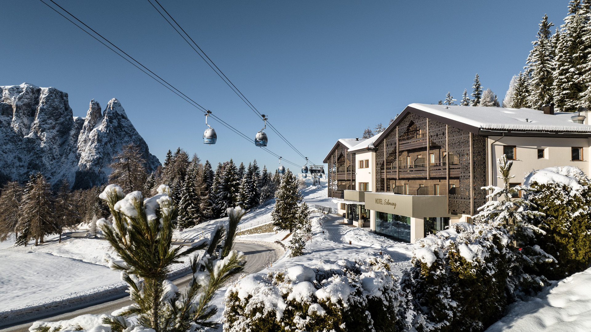 Hotel Schmung – Ihr Hotel auf der Seiser Alm Verschneites Berghotel mit Seilbahn vor einer schroffen Bergkulisse